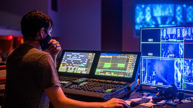 Man sitting in front of a video production switcher with mask on